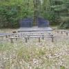 View 1 of several benches sitting in front of a small stage with trees in the background.