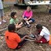 Three students and one adult sit in a circle outside and talk.