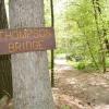 A sign that says "Thompson Bridge" is nailed to a tree next to a path leading up to a small bridge.