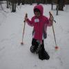 A young girl wearing a bright pink jacket snowshoes through the woods.