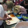 Two young girls slice carrots and celery.