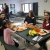 Two students and two adults cut carrots while sitting at a table together.