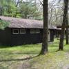 A brown shower building in the foreground and screened-in Jack Pine Pavilion in the background, surrounded by trees.