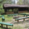 A campfire area surrounded by seven long, green benches with a screened in building in the background.