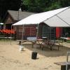 A white awning and picnic table sits in front of a boat house and wooden fence lined with red life vests.