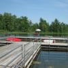 A lifeguard stands on a large wooden dock lined with metal railings and a small pool in the center.