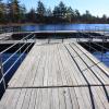 A large wooden dock on a lake in summer, featuring metal railings on the sides and a small pool area in the center.