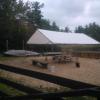 A white awning covers a picnic bench in a small sand-filled area next to a lake.