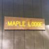 Brown sign that reads "Maple Lodge" in yellow.