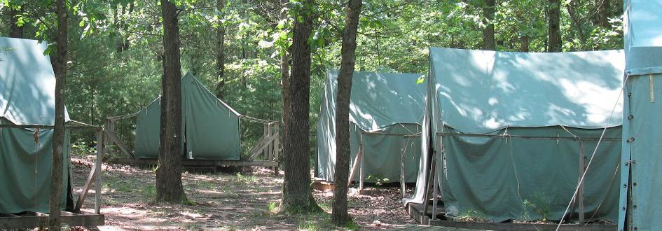 Five large green tents arranged in a circle on platforms.