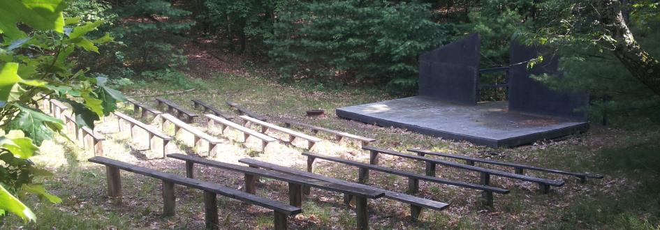Rows of benches sit in front of a small wooden platform with a black backdrop.