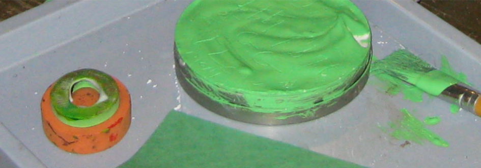 Green and orange cylindrical pieces rest next to a paintbrush with green paint.
